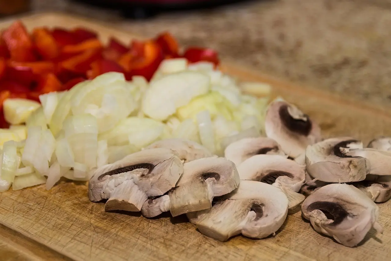 Skivede champignoner, hakket løg og peberfrugt klar på et skærebræt